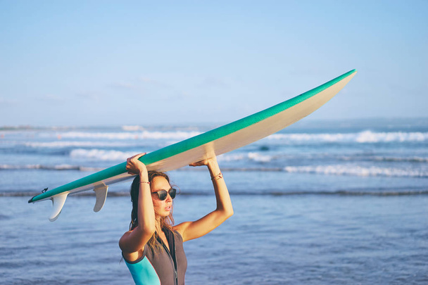 Pretty young woman holding surf board on the sea beach. - Фото, изображение