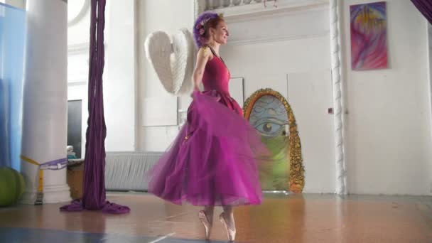 Jonge mooie ballerina in paarse jurk voert dans in ruime witte studio - Video
