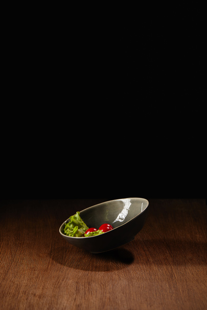 Tomates mûres et feuilles de salade dans un bol sur une table en bois
  - Photo, image