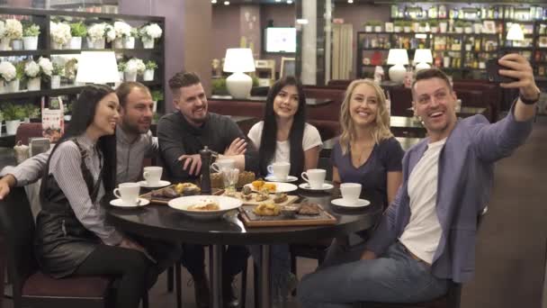 μια μεγάλη ομάδα φίλων κάνει μια selfie που κάθεται σε ένα τραπέζι σε μια καφετέρια ή εστιατόριο. - Πλάνα, βίντεο