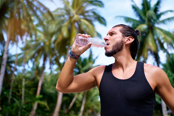 Handsome strong young man drinking water outdoors. - Foto, imagen