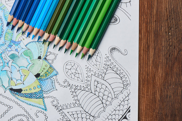 coloring page with pencils in blue and green colors on wooden table , close-up  - Foto, imagen
