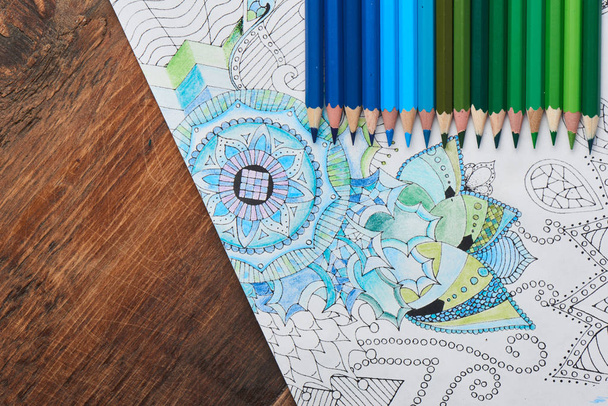 coloring page with pencils in blue and green colors on wooden table , close-up  - Foto, imagen