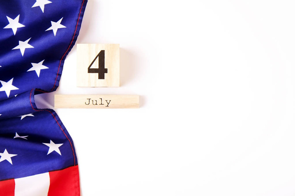 Ruffled American flag and wooden cube calendar with 4th of July date. Happy Independence Day greeting card template on white copy space background. US patriotic festive composition, top view, close up - Foto, immagini