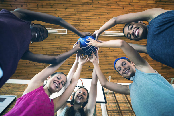 Low angle view of smiling high school kids holding basketball together in the court - Fotografie, Obrázek