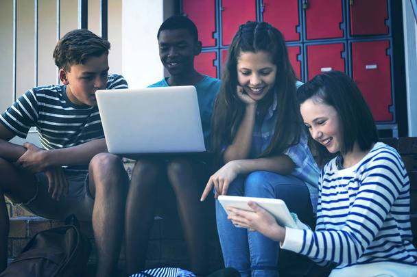 Schüler nutzen Laptop, Handy und digitales Tablet im Treppenhaus der Schule - Foto, Bild