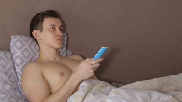 Yakışıklı adam yatakta yatıyordu bir Tv Uzaktan kumanda ile. - Fotoğraf, Görsel