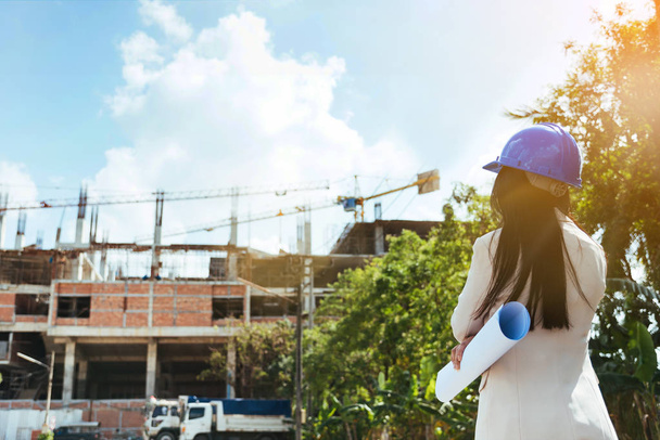 Asian woman architect wearing blue safety helmet checking working progress at contruction site. - Fotó, kép