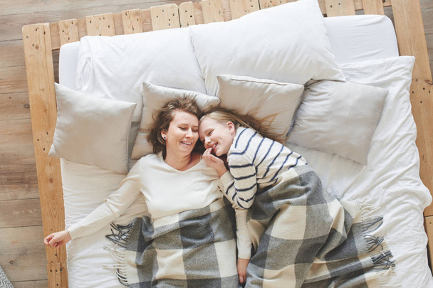 Mom and daughter lying in white bed among pillows at home - Foto, afbeelding