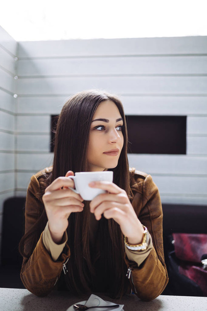 Ładna Brunetka młoda kobieta siedzi w barze-kawiarni i picia kawy.  - Zdjęcie, obraz