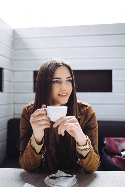 Kaunis brunette nuori nainen istuu kahvilassa baarissa ja juo kahvia
.  - Valokuva, kuva