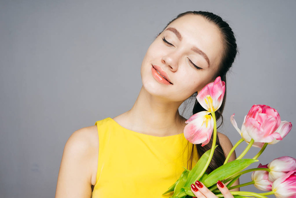 a peaceful young girl in a yellow dress is holding a bouquet of fragrant flowers, closed her eyes and smiles - Foto, Imagen