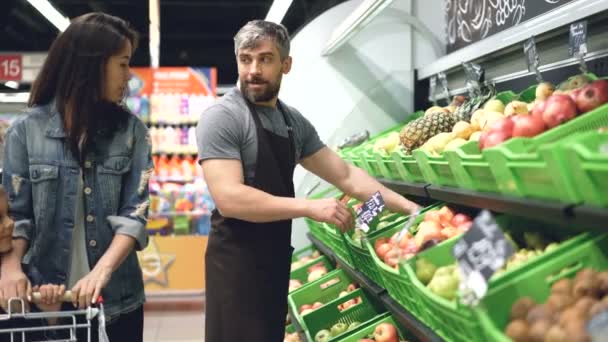 Attractive woman interested customer is talking to handsome guy friendly salesman working in fruit department in supermarket, woman is smelling fresh fruit. - Filmati, video