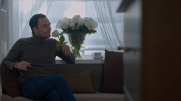Man smells a rose and dreaming about his wife in the living room - Foto, Imagen