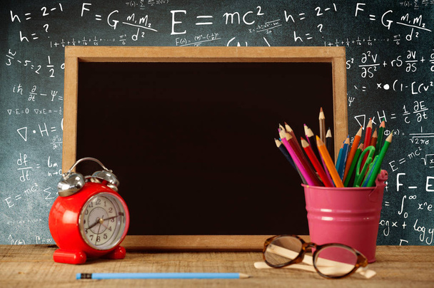 Slate with desk organizer and alarm clock by eyeglasses against empty blackboard in school - Foto, afbeelding