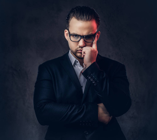 Retrato de cerca de un hombre de negocios con estilo reflexivo con cara seria en un elegante traje formal y gafas sobre un fondo oscuro
. - Foto, Imagen