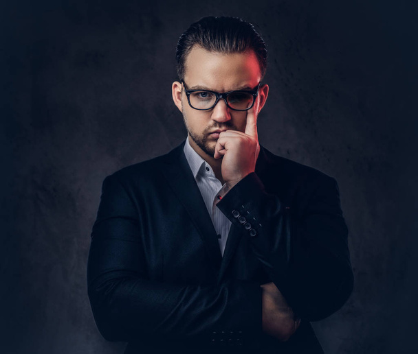 Egy átgondolt elegáns üzletember egy elegáns formális ruha és szemüveg sötét háttér előtt komoly arccal közeli portréja. - Fotó, kép