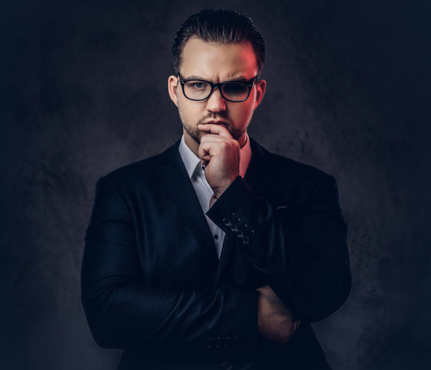 Retrato de cerca de un hombre de negocios con estilo reflexivo con cara seria en un elegante traje formal y gafas sobre un fondo oscuro
. - Foto, Imagen