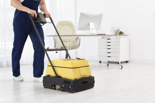 Male worker with floor cleaning machine indoors - Foto, afbeelding