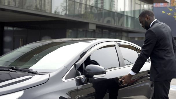 El hombre afroamericano abre cuidadosamente la puerta del coche nuevo antes de salir del estacionamiento
 - Foto, imagen