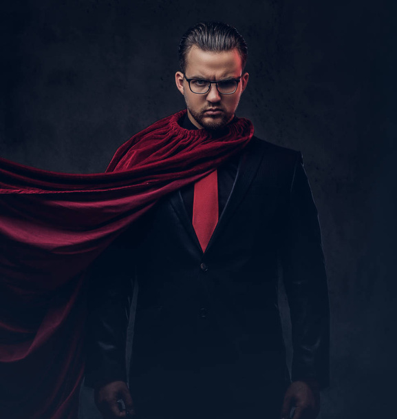 Porträt eines genialen Superhelden im schwarzen Anzug mit roter Krawatte auf dunklem Hintergrund.  - Foto, Bild