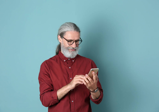 Handsome mature man with mobile phone on color background - Zdjęcie, obraz