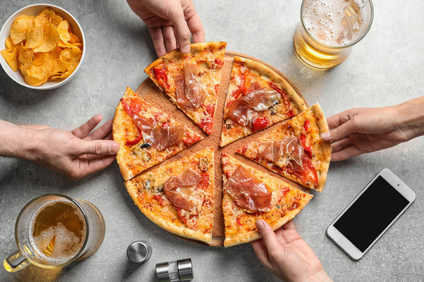Young people taking slices of tasty pizza with meat at table, top view - Foto, afbeelding