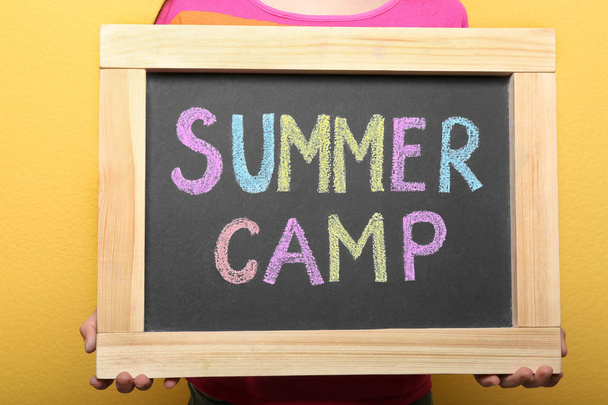 Child holding blackboard with words SUMMER CAMP chalked in different colors, closeup - 写真・画像