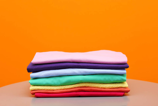 Stack of rainbow clothes on table against color background - Foto, immagini