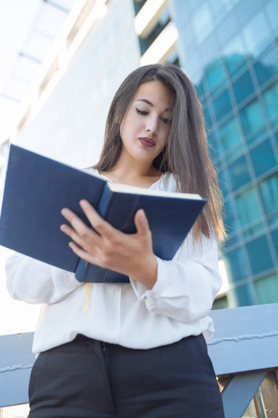 Business woman portrait outdoors writing notes, with modern building as background - Photo, image