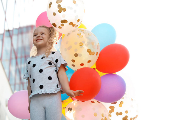 Cute little girl with colorful balloons outdoors on sunny day - 写真・画像