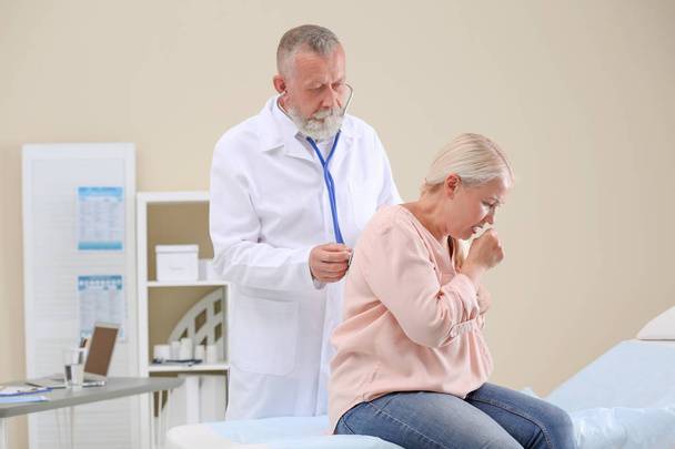 Doctor examining coughing mature woman at clinic - Фото, изображение
