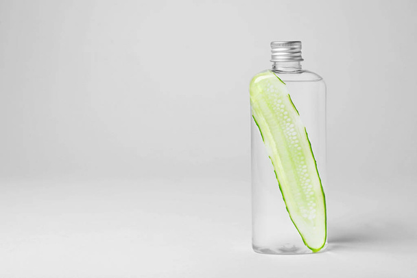 Bottle with cucumber water on light background. Fresh skin care tonic - Фото, изображение
