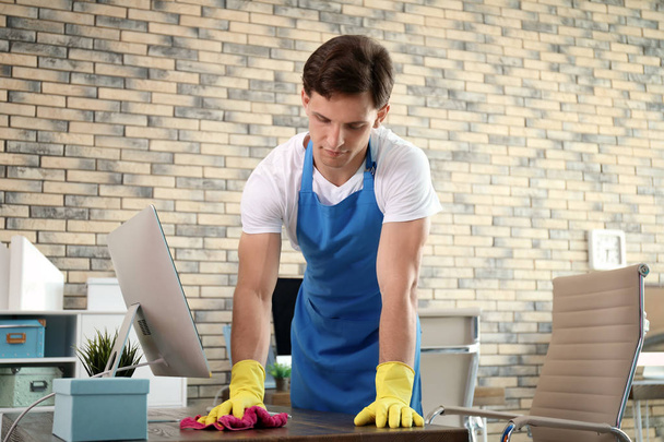 Young man in apron and gloves cleaning office - Фото, изображение