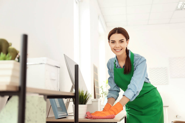 Young woman in apron and gloves cleaning office - Фото, изображение