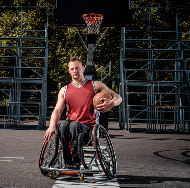 Retrato de um jogador de basquete com deficiência em uma cadeira de rodas em um campo de jogos aberto
. - Foto, Imagem