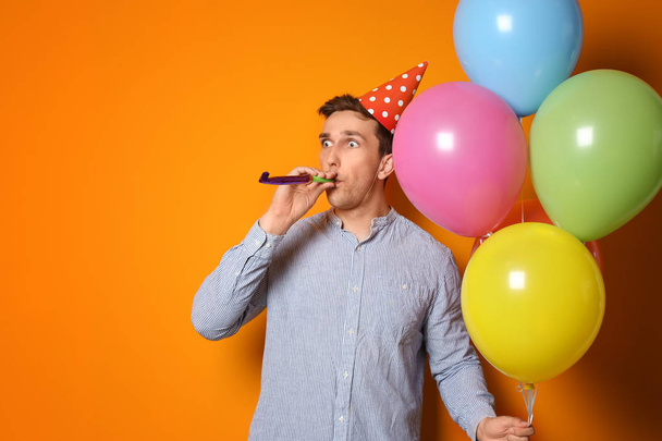 Young man with bright balloons and party blower on color background. Birthday celebration - Фото, зображення
