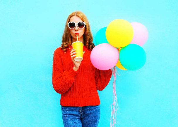Funny girl with an air balloons holds cup of fruit juice on blue background - Fotografie, Obrázek