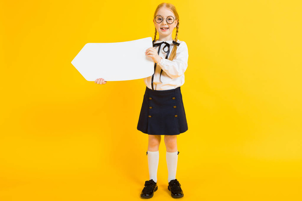 Κορίτσι με κόκκινο κοτσίδες σε κίτρινο φόντο. Ένα γοητευτικό κορίτσι με γύρο διαφανή ποτήρια κρατάει ένα λευκό πλαίσιο κειμένου. - Φωτογραφία, εικόνα