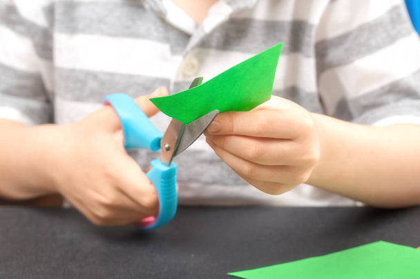 Cutting out of colored paper. A child with an end-point scissors cuts green paper. The concept of childrens creativity, learning, quiet games and the development of creative thinking - Photo, Image