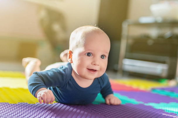 Portrait of cute caucasian baby boy crawling on soft playing mat indoors. Adorable child having fun making making first steps on floor at nursery. Backlit.  Happy childhood and evolution concept. - Photo, Image