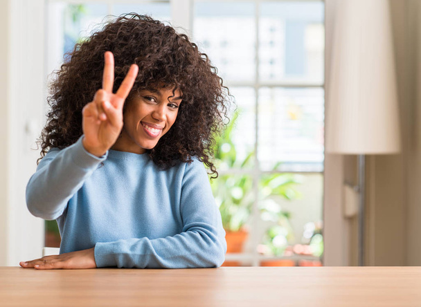 Mujer afroamericana en casa sonriendo mirando a la cámara mostrando los dedos haciendo señal de victoria. Número dos.
. - Foto, Imagen