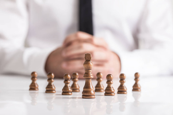 Businessman with clasped hands planning strategy with dark chess figures on white table. - Photo, Image