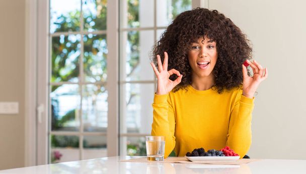 Ok işareti parmaklar, mükemmel sembolü ile Afrikalı-Amerikalı kadın ahududu ve yaban mersini evde yemek yapıyor - Fotoğraf, Görsel