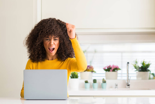 afrikanisch-amerikanische Frau mit Computer-Laptop in der Küche genervt und frustriert schreien vor Wut, verrückt und schreien mit erhobener Hand, Wut Konzept - Foto, Bild