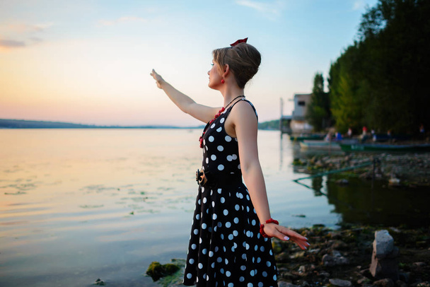 Egy gyönyörű fiatal nő felöltözve állt a tó, a háttérben a naplemente. - Fotó, kép