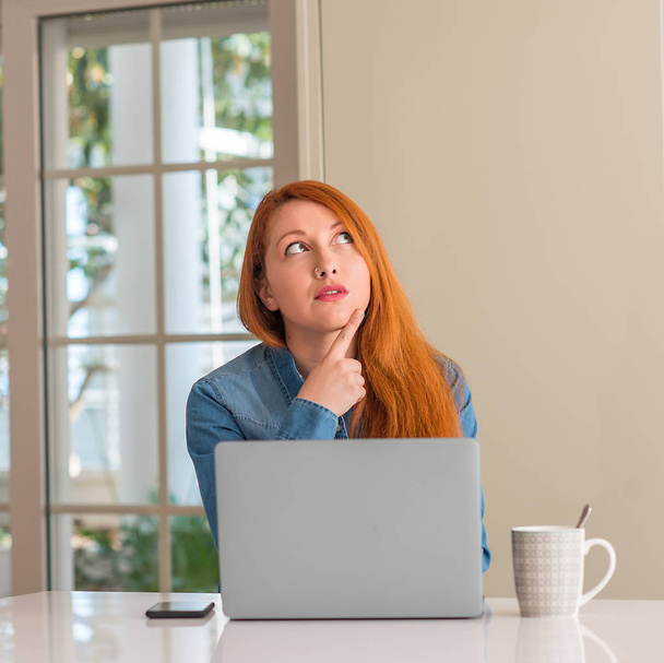 Femme rousse utilisant un ordinateur portable à la maison visage sérieux penser à la question, idée très confuse
 - Photo, image