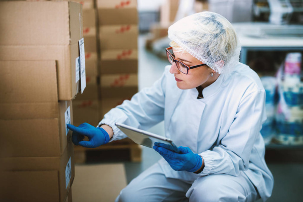 junge schöne Arbeiterin in steriler Kleidung mit Tablette in der Fabrik - Foto, Bild