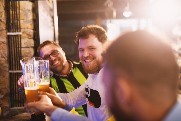 Happy ποδόσφαιρο οπαδούς πίνοντας μπύρα σε παμπ και τσούγκριζαν ποτήρια  - Φωτογραφία, εικόνα