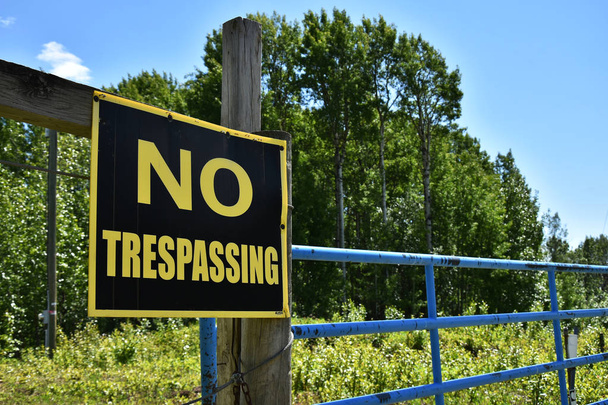 An image of an old yellow and black no trespassing sign posted on a wooden fence post.  - Photo, Image